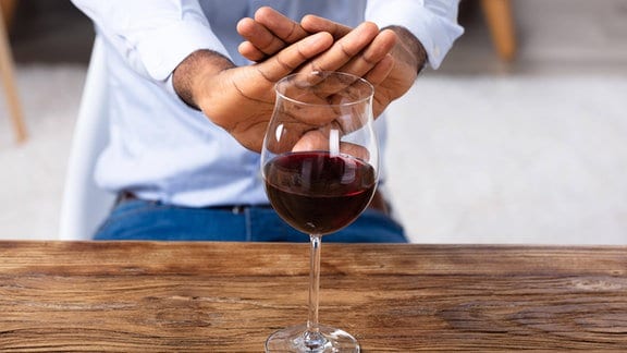 Ein Mann hält beide Hände in einer abwehrenden Geste in Richtung eines Weinglases.