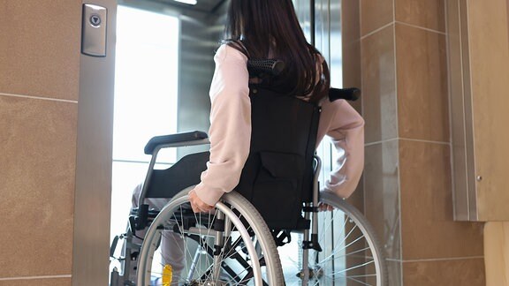 Eine junge Frau fährt in einem Rollstuhl in einen Fahrstuhl