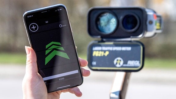 Ein Mobiltelefon mit einer Radarwarn-App wird vor eine Lasermesspistole der Polizei gehalten