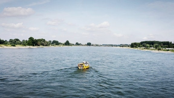 Ein gelbes Boot fährt auf einem breiten Fluss.