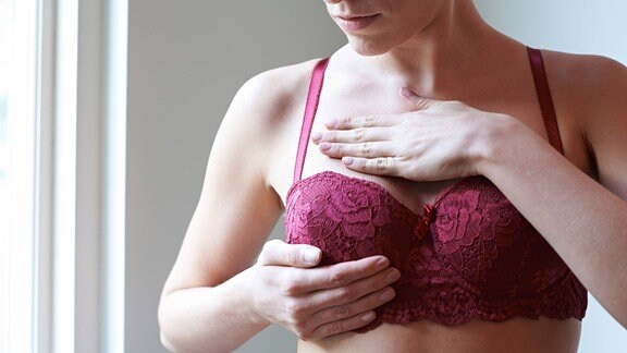 Eine Frau im BH untersucht ihre Brust.