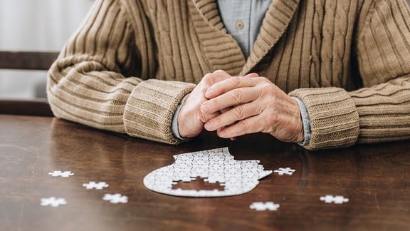 Ausgeschnittene Ansicht eines Rentners, der ein Puzzles auf dem Tisch liegen hat