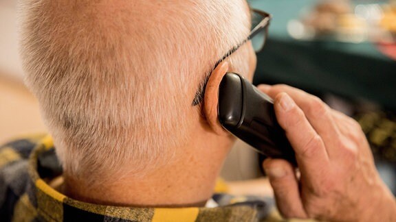 Ein älterer Herrr hält ein Telefon an seinem Ohr.