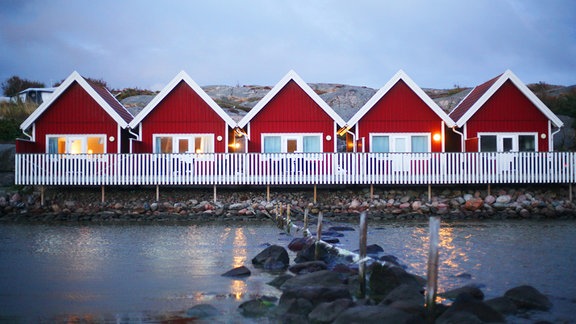 Rote Schwedenhäuschen aus Holz stehen am Wasser in der Abenddämmerung auf einem Campingplatz in der Nähe von Kungsham an der Westküste von Schweden.