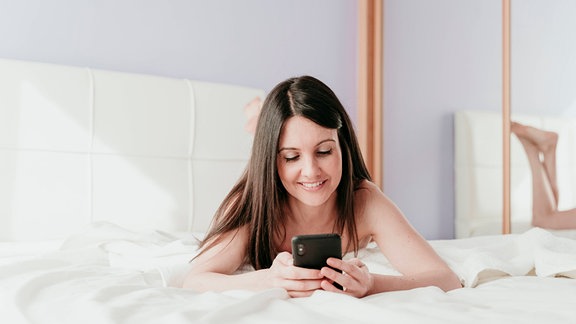 Frau liegt mit Handy auf einem Bett