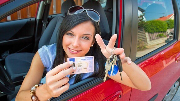 Frau mit neuem Auto und Führerschein und Autoschlüssel