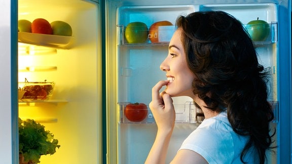 Eine junge Frau sieht in einen Kühlschrrank