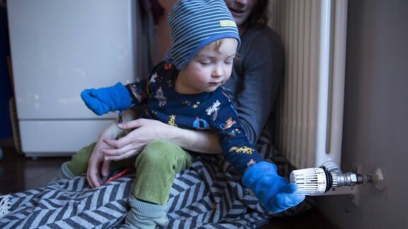 Ein Kind mit Handschuhen dreht an einer Heizung