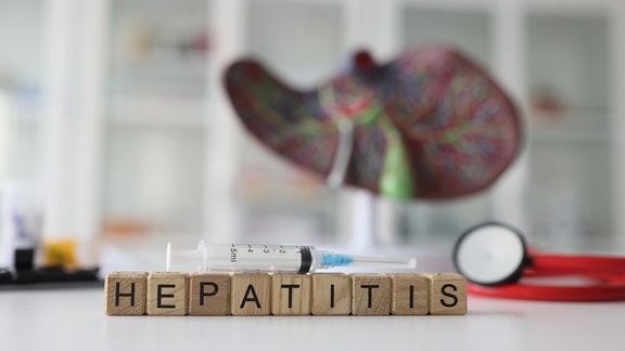 Eine Spritze liegt auf Buaklötzen mit Buchstaben auf den Hepatitis steht.
