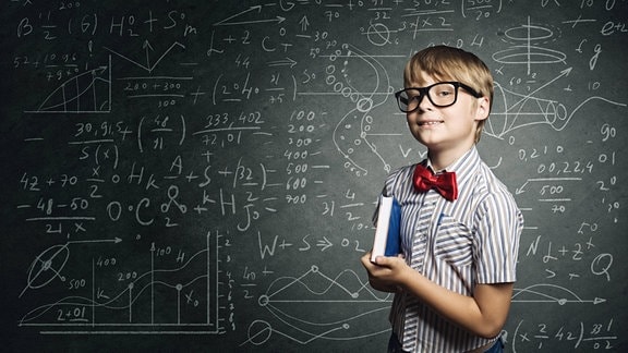 Ein Kind steht vor einer Tafel mit mathematischen Formeln, Symbolbild