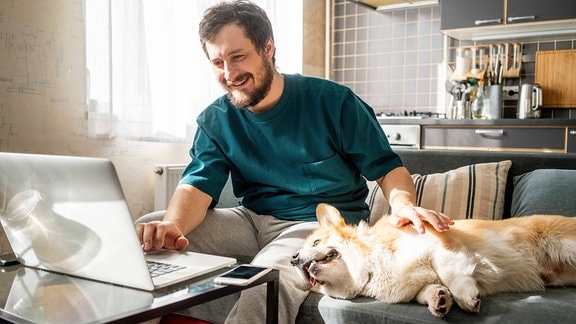 Mann mit Hund auf Sofa an Laptop