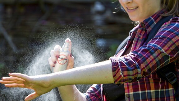 Junge Frau trägt vor einer Wanderung ein Insektenschutz-Spray auf die Haut auf.