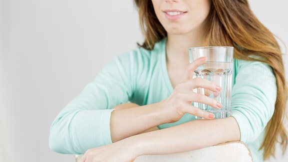 Eine junge Frau mit einem großen Glas Wasser in der Hand.