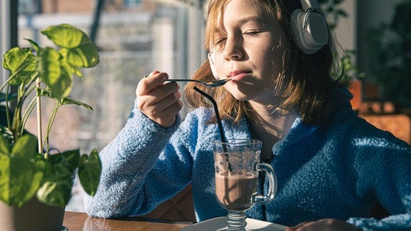 Mädchen mit Kopfhörern mit einem Glas Kakao