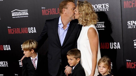 Kevin Costner mit Familie bei einem Empfang, Costner küsst seine Ehefrau.
