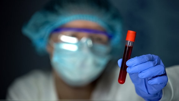 Person in Laborkleidung hält Reagenzglas mit Blut