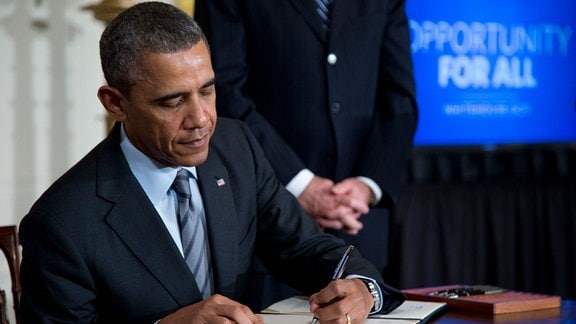 Barack Obama unerzeichnet ein Dokument mit der linken Hand.