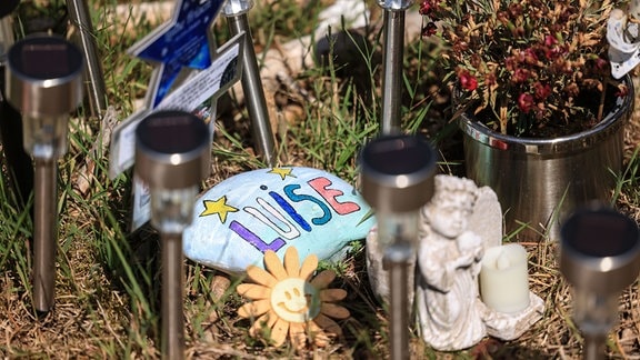 Eine Steine, Blumen und Lichter stehen am Waldrand an der Stelle, an der das Mädchen Luise tot gefunden wurde.