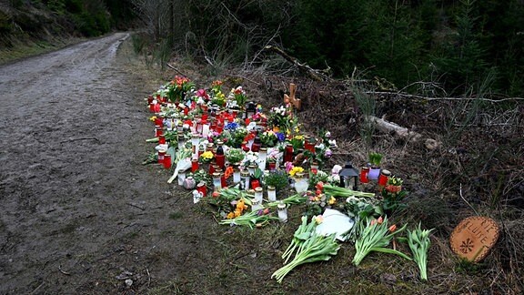 Ein Holzkreuz, zahlreiche Blumen, Kuscheltiere und Kerzen liegen am Tatort.