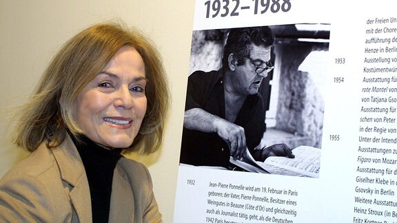 Margit Saad-Ponnelle steht 2002 neben einem Bild des Regisseurs, Bühnen- und Kostümbildners Jean-Pierre Ponnelle.