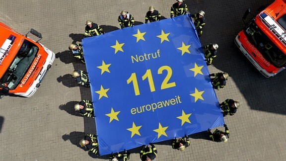 Feuerwehrmänner der Feuerwache 1 in Stuttgart halten eine Fahne mit der Aufschrift «Notruf 112 europaweit»