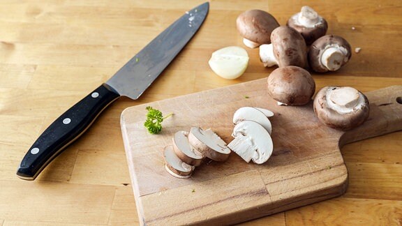 Pilze im Ganzen und in Scheiben geschnitten auf einem Holzbrett und einem Küchenmesser.