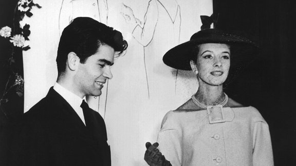 Ein junger Karl Lagerfeld neben einem Model, das Mode von ihm trägt.