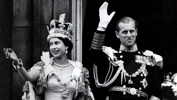 Die britische Königin Elizabeth II mit Krone und ihr Mann Prinz Philip, Herzog von Edinburgh (in der Uniform eines Marine-Admirals), winken nach der prunkvollen Krönungszeremonie in der Westminster-Abtei in London am 02.06.1953 vom Balkon des Buckingham Palasts den Menschen zu. 
