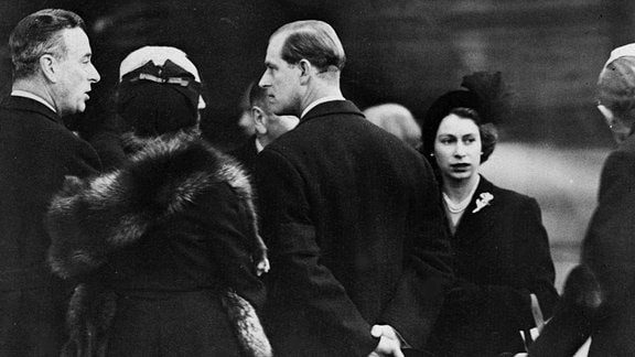 Historisches Schwarzweiß-Foto: Königin Elizabeth II. und Prinz Philip werden 1952 auf dem Flughafen London begrüßt.