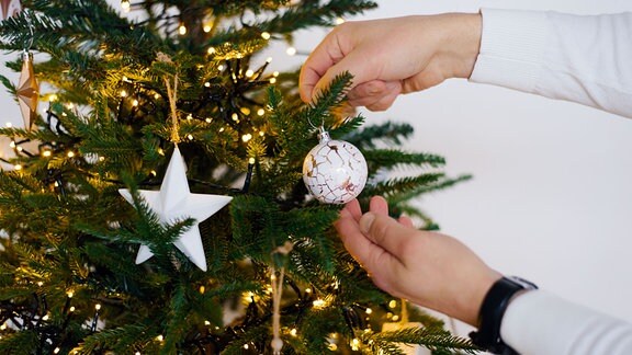 Ein Mann hängt eine Kugel an einen Weihnachtsbaum