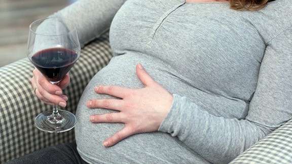 ILLUSTRATION - Eine schwangere Frau sitzt in einer Wohnung und haelt ein Glas mit Rotwein (gestellte Szene).