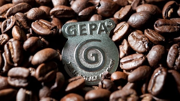 Ein Logo der GEPA zwischen ganzen, losen Kaffeebohnen