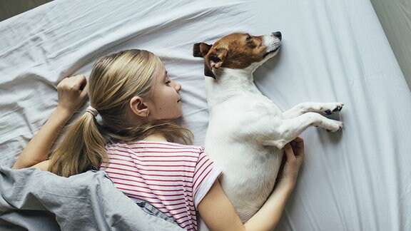 Ein Blondes Mädchen liegt mti einem Hund auf einem Bett