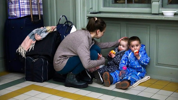 Eine Mutter mit Kindern ruht sich in einem provisorischen Unterstand in einem Bahnhofsgebäude aus.