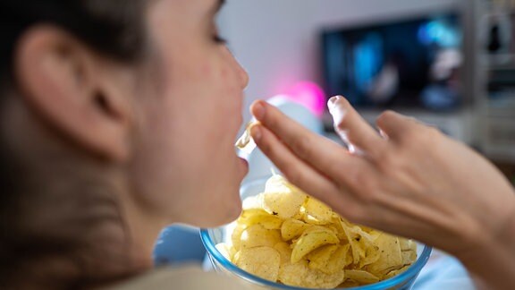 Eine Frau isst in einem Wohnzimmer vor dem Fernseher Chips.