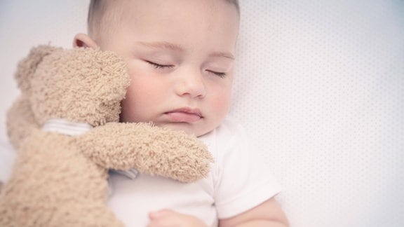 Ein Kind schläft mit einem Teddybär im Arm.