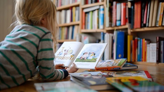Ein Kind liegt zwischen vielen Büchern und schaut sich ein Buch an.