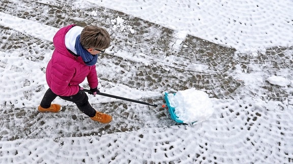 Nach den milden letzten Tagen ist der Winter zurueck im Siegerland, eine Frau mit pinker Jacke schiebt Schnee, befreit das Grundstueck vom Schnee in Siegen-Oberschelden Winter im Siegerland am 24.01.2021 in Siegen/Deutschland.