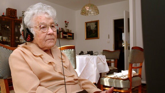 Schwerhörige alte Frau sitzt mit Kopfhörern vor dem Fernseher