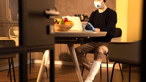 Ein Mann mit Gipsbein sitzt an einem Tisch vor einem Laptop