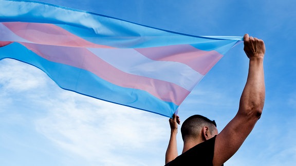 Eine Person hält eine transgender pride Flagge hoch.