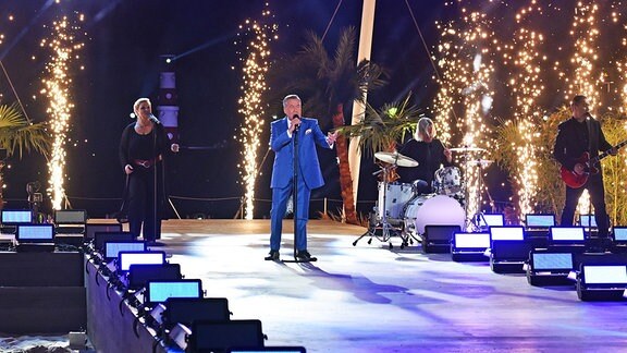 Roland Kaiser sing in dunkelblauem Anzug auf der Bühne, im Hintergund Feuerspeier.
