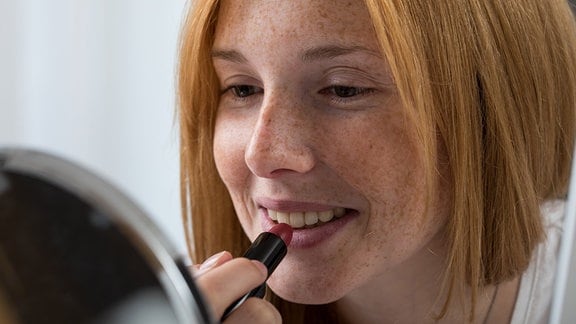 Eine junge Frau benutzt in einer Wohnung einen Lippenstift (gestellte Szene)
