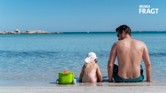 Kleines Mädchen sitzt mit seinem Vater im flachen Meerwassser.