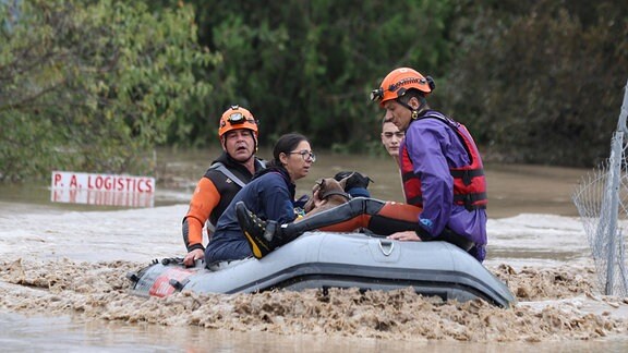 Feuerwehrleute mit einem Schlauchboot evakuieren Menschen aus einem überfluteten Gebiet. 