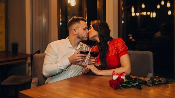 Symbolbild: Ein Liebespaar gibt sich einen Kuss an einem Tisch im Restaurant
