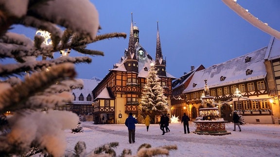 Menschen gehen über den schneebedeckten Marktplatz mit dem Rathaus 