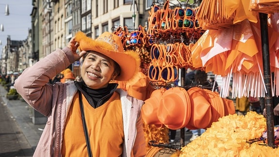 Frau mit orangenem Shirt und Hut neben Stand mit weteren orangenen Accessoires