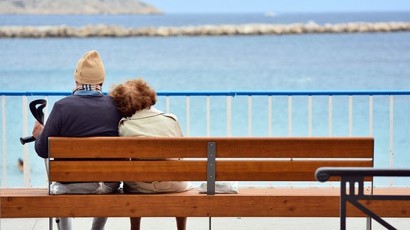 Älteres Ehepaar sitzt auf Bank am Strand.