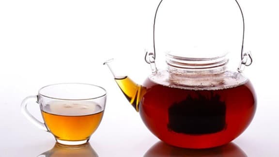 Eine gläserne Teekanne ist gefüllt mit rotem Tee. Neben dieser steht ein Teetasse aus Glas, welche ebenfalls mit Tee gefüllt ist.